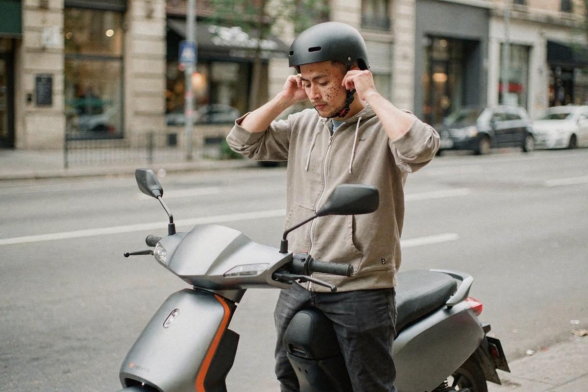 Rider fastening a helmet next to an electric scooter on a city street before setting off